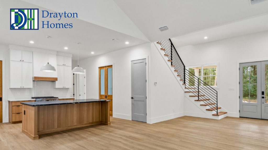 Custom open concept kitchen and living area featuring white cabinets a wood island and a modern staircase built by Drayton Homes in Baldwin County AL